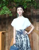 吴谨言身着白色上衣与椰树印花长裙，手扶椅背亭亭玉立，尽显优雅身姿