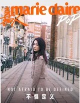孟美岐身着个性拼接外套靠坐街边，阳光洒落肩头发梢，流露出不经意间的惬意与洒脱