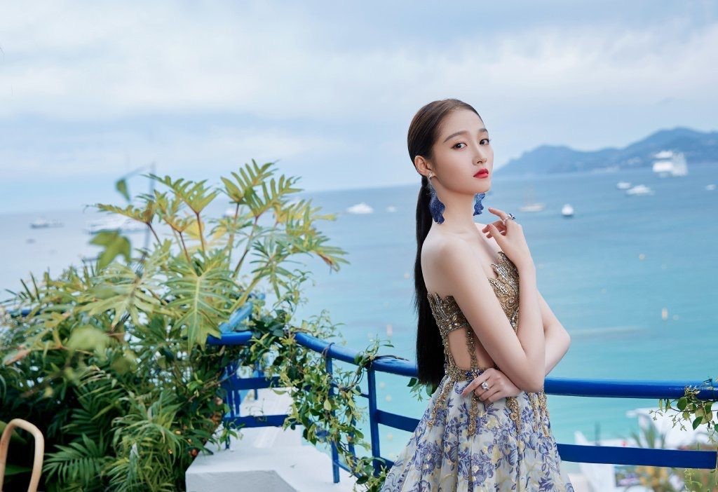 关晓彤身着白色无袖连衣裙，宛如林间精灵赤足漫步于葱郁草地，发丝随风轻扬，眼神清澈含笑。