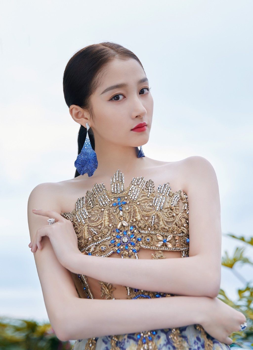 关晓彤侧身倚靠，一袭酒红色吊带长裙勾勒出优雅曲线，背景是暮色中的蔚蓝海岸，风情万种。