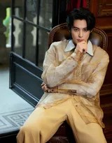 王鹤棣坐在高脚凳上，双腿随意交叠，一手轻搭膝头，姿态松弛而优雅，展现自信从容的型格