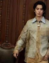 王鹤棣倚靠于复古砖墙前，浅棕衬衫与背景色调和谐相融，他微仰着头，眼神放空，陷入沉思