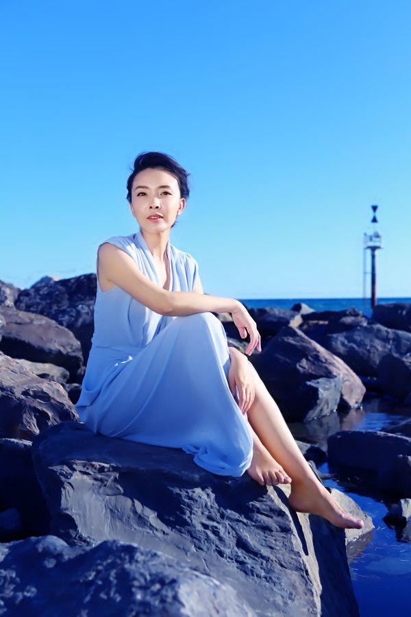侧身立于海边的刘威葳，一袭露背白色长裙勾勒出优雅身形，海风轻拂发丝，她望向远方，眼神沉静而深远