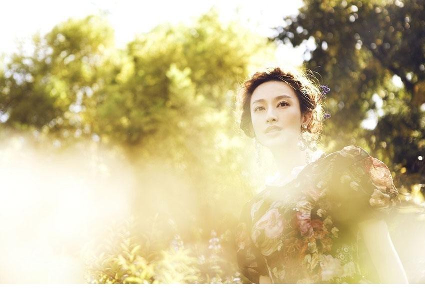 张俪闭目轻嗅手中花香，神情专注而宁静，仿佛与周围自然融为一体