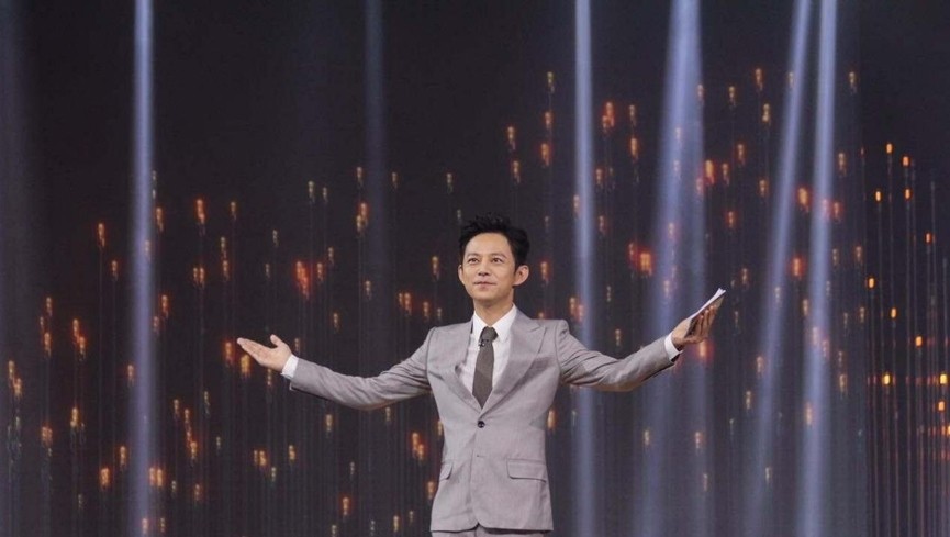 何炅在快乐大本营舞台上手持麦克风与嘉宾互动的全身照